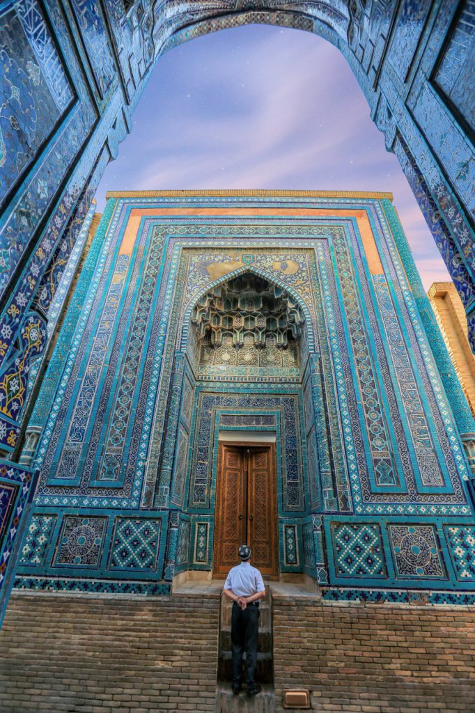 Voyageur face à un portail monumental couvert de mosaïques bleues à Samarcande.