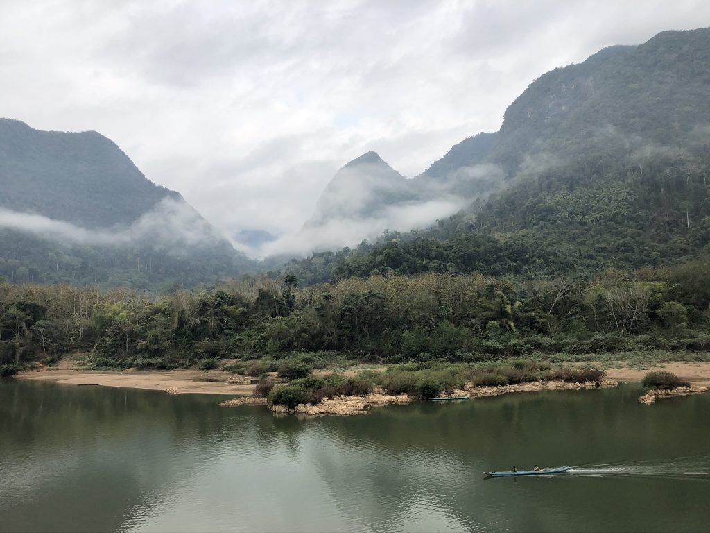 Rivière paisible au pied de montagnes couvertes de brume au Laos.